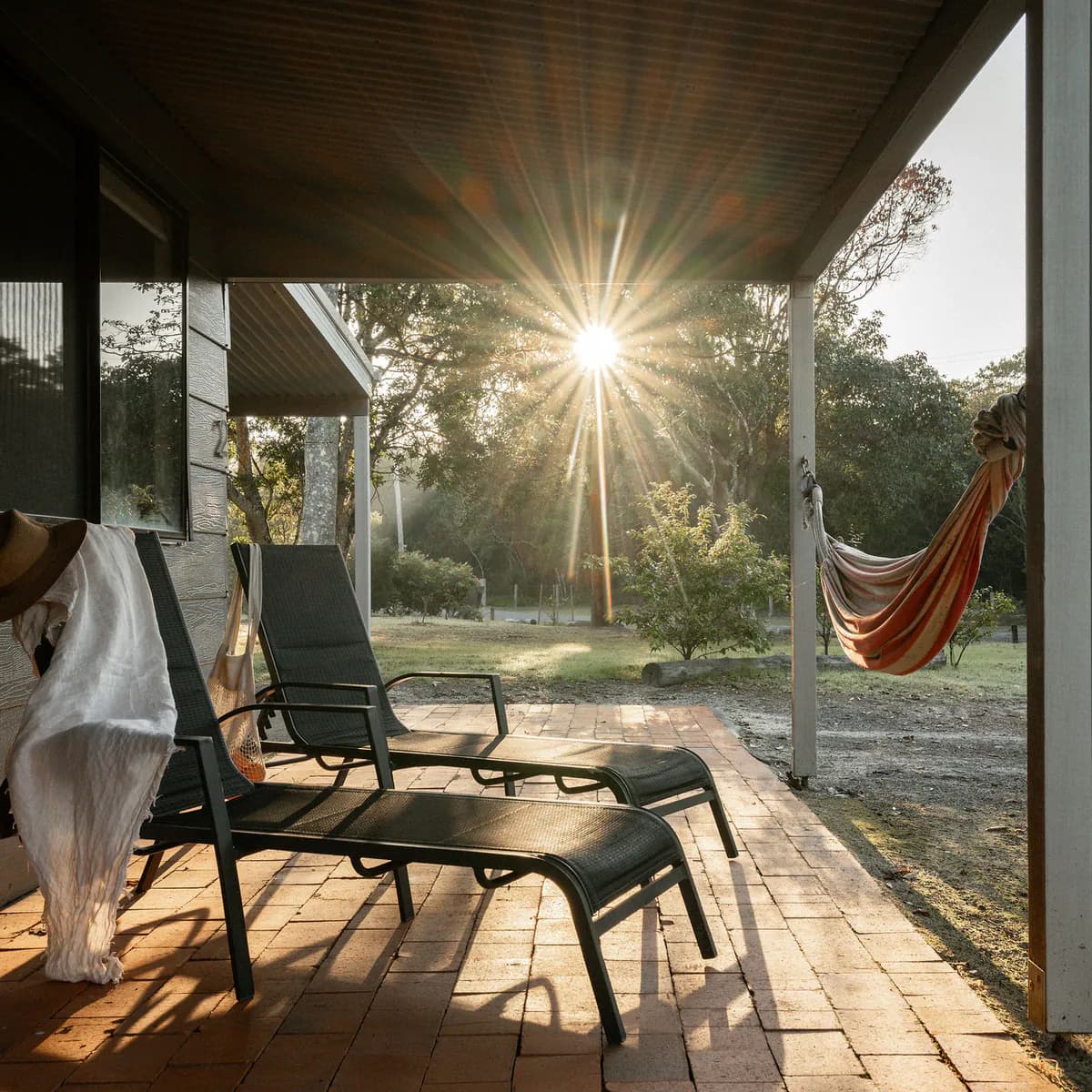 Sun loungers and a hammock on a cottage verandah at golden hour
