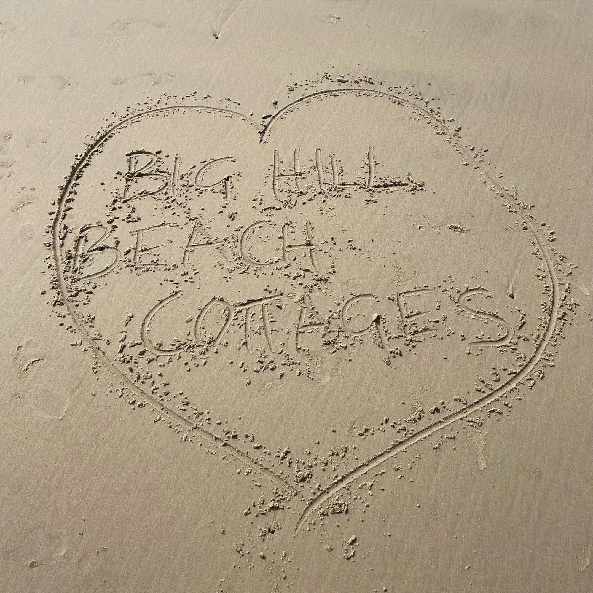 Big Hill Beach Cottages written in the sand inside a heart